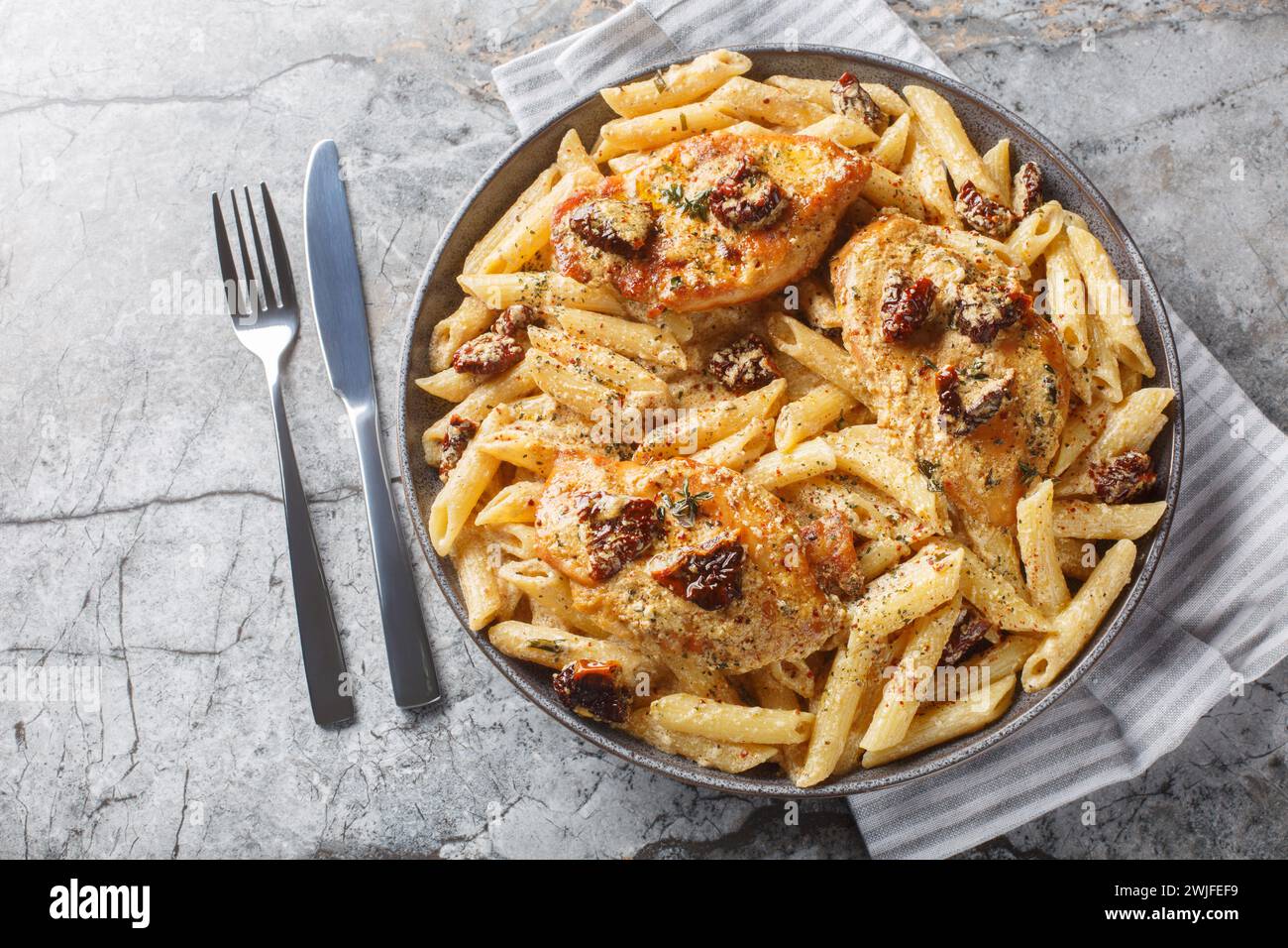 Creamy Marry Me Chicken pasta with sun-dried tomatoes, cheese, herbs and aromatic sauce close-up in a plate on a marble table. Horizontal top view fro Stock Photo