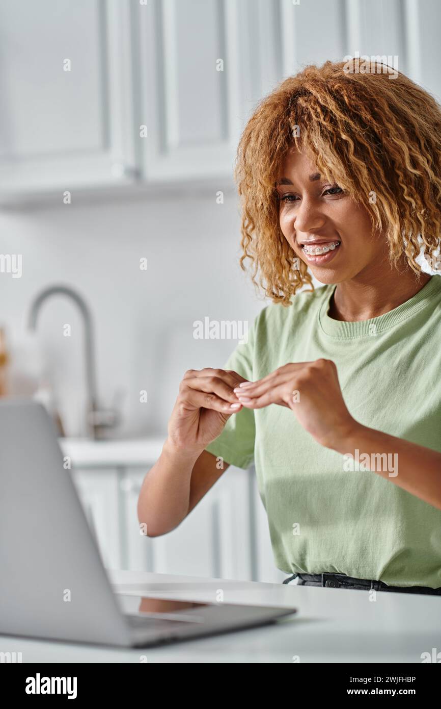 happy african american woman in braces using sign language during video