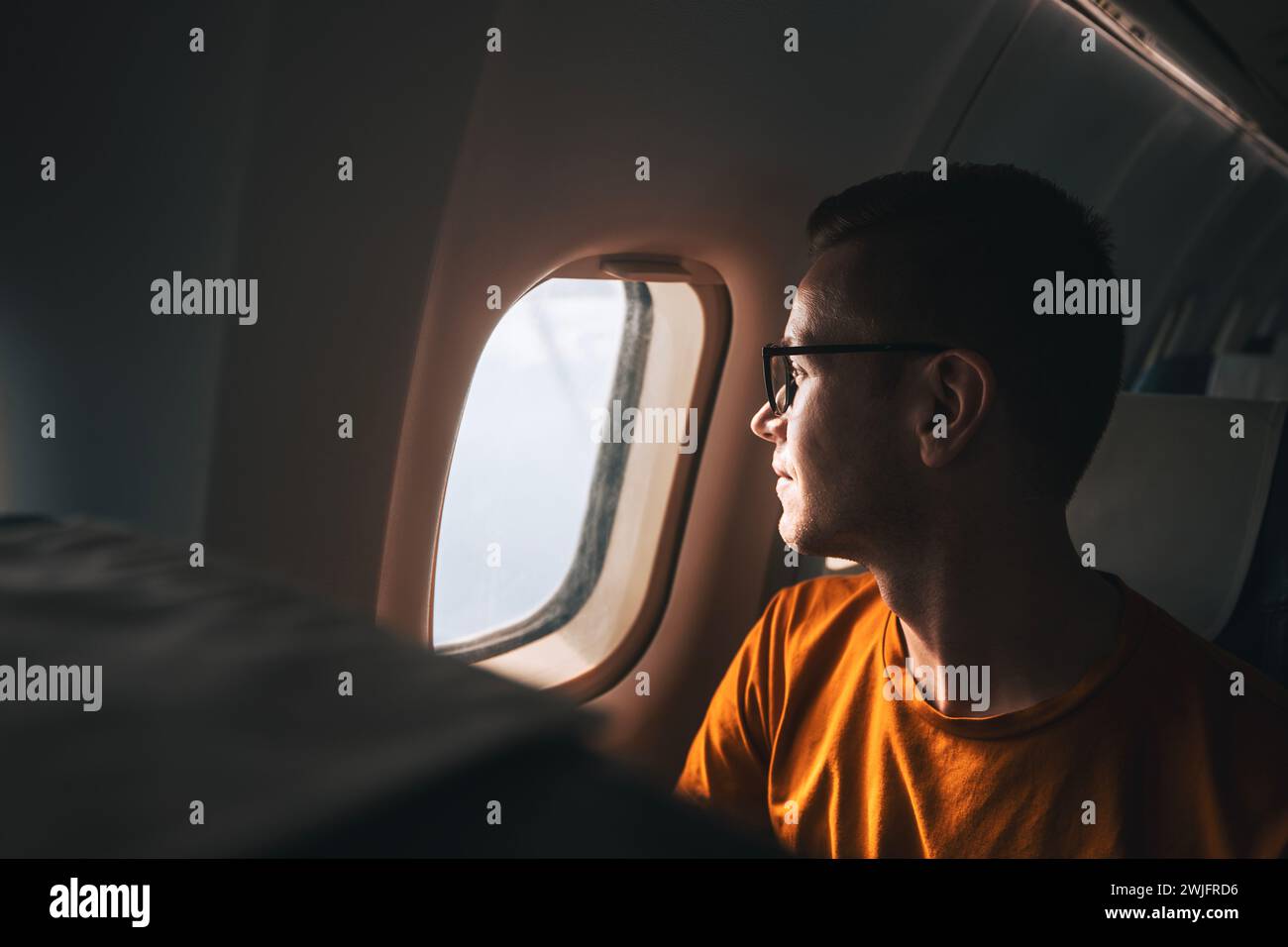 Portrait of man traveling by airplane. Passenger looking through plane window during flight. Stock Photo