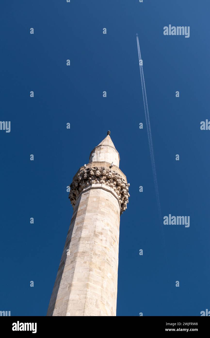 Mosque minaret against blue sky, flying plane leaving chemtrail Stock Photo