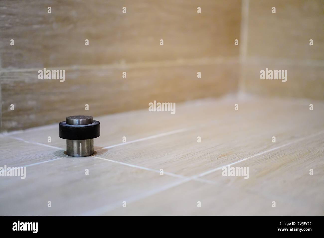 Stainless door stop with black rubber behind the door on the floor. Protection of walls, baseboards against door impact damage Stock Photo