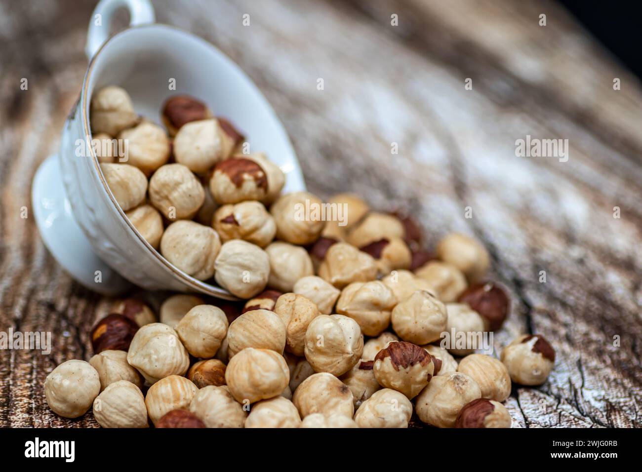 Peeled and roasted organically grown hazelnuts spilling out of a ceramic bowl on wooden table, close-up of healthy roasted hazelnuts, healthy snacks Stock Photo