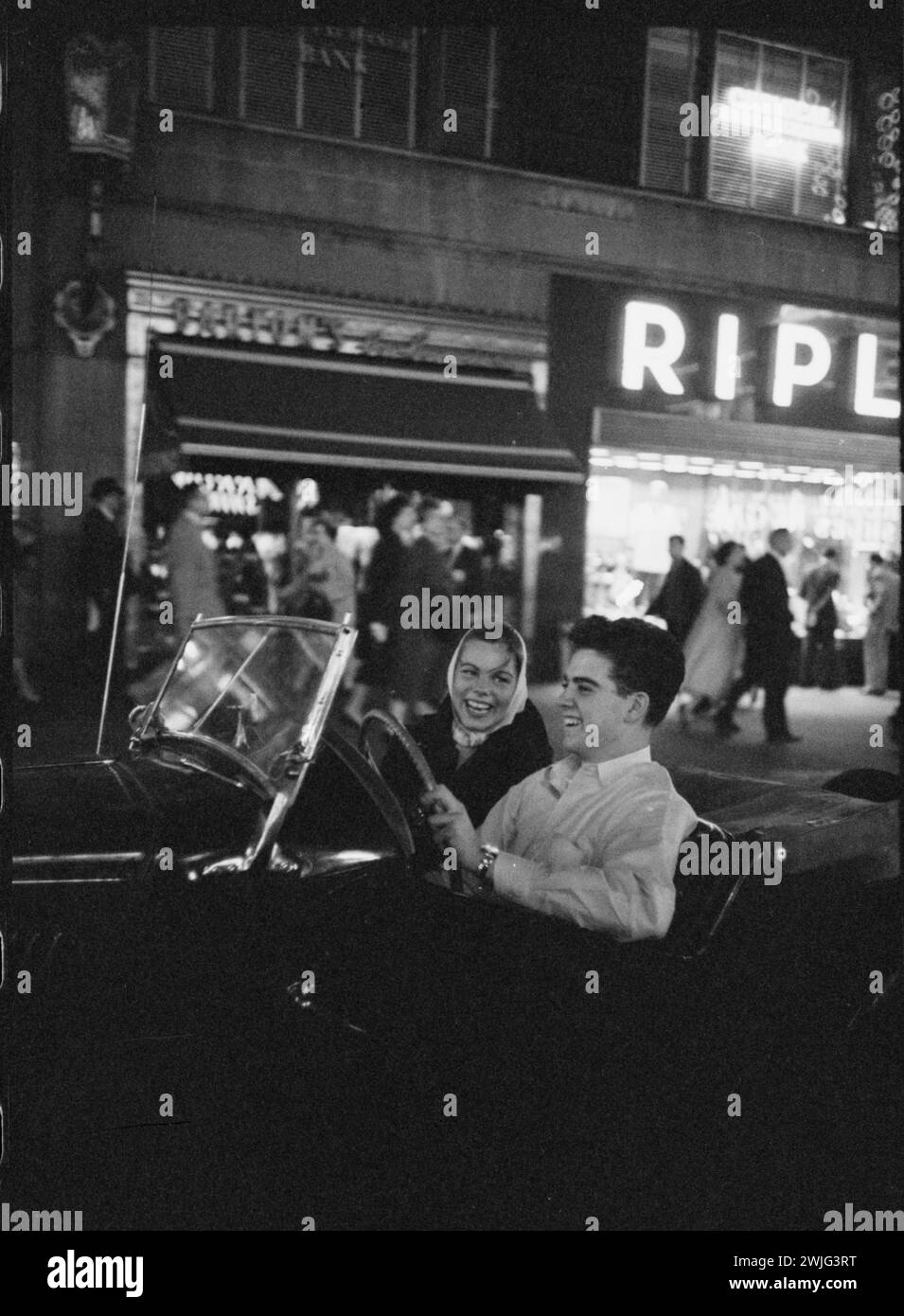 Teen driver Bill Kolb driving his unidentified date in an MG convertible through the downtown area of White Plains, White Plains, New York, circa 1958. (Photo by Charlotte Brooks/LOOK Magazine Collection/LOC) Stock Photo