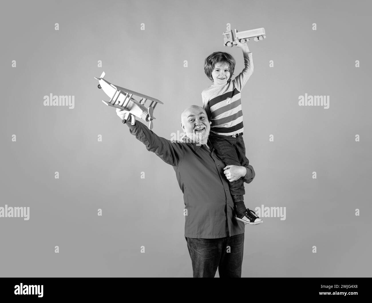 Child boy and grandfather piggyback with toy plane and wooden truck