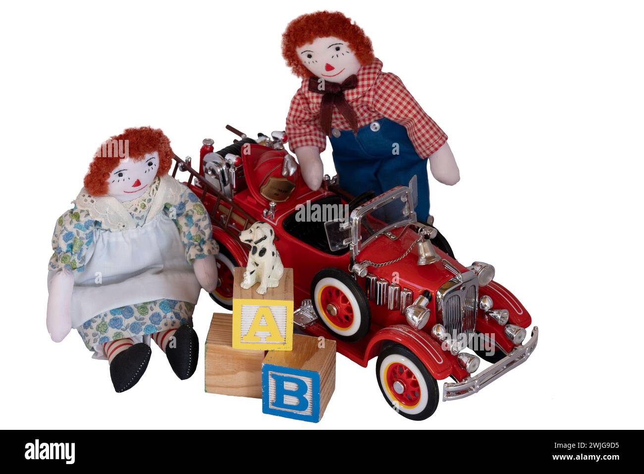 Handmade rag dolls, Raggedy Ann & Andy placed among toys, blocks, fire engine, little dog, fireman hat, old & newer toys in wood and metal. Isolated Stock Photo