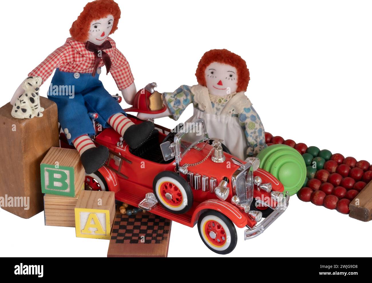 Handmade rag dolls, Raggedy Ann & Andy placed among toys, blocks, fire engine, little dog, fireman hat, old & newer toys in wood and metal. Isolated Stock Photo