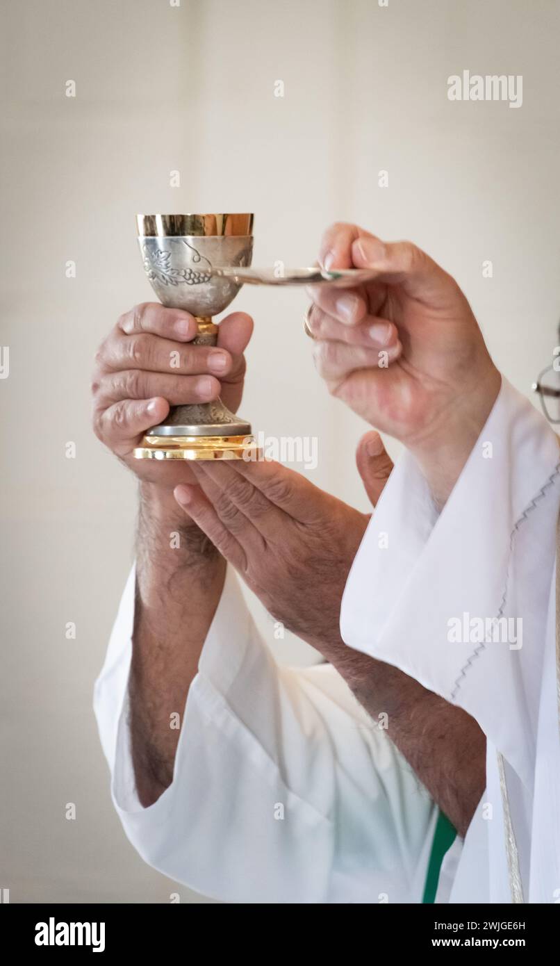 Close-up shot of the hands of a priest holding aloft a Host and Chalice during a Catholic mass. Stock Photo