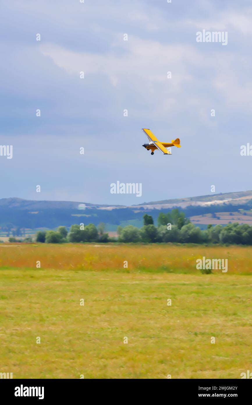 Yellow single engine airplane maneuvering close to the ground with cloudy sky at the background Stock Photo