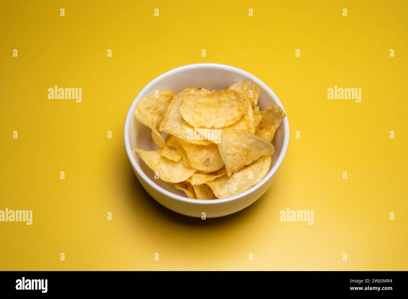 , Food, Deutschland, 15.02.2024,  Weißer Schale voller goldener Kartoffelchips auf gelbem Hintergrund. Stock Photo