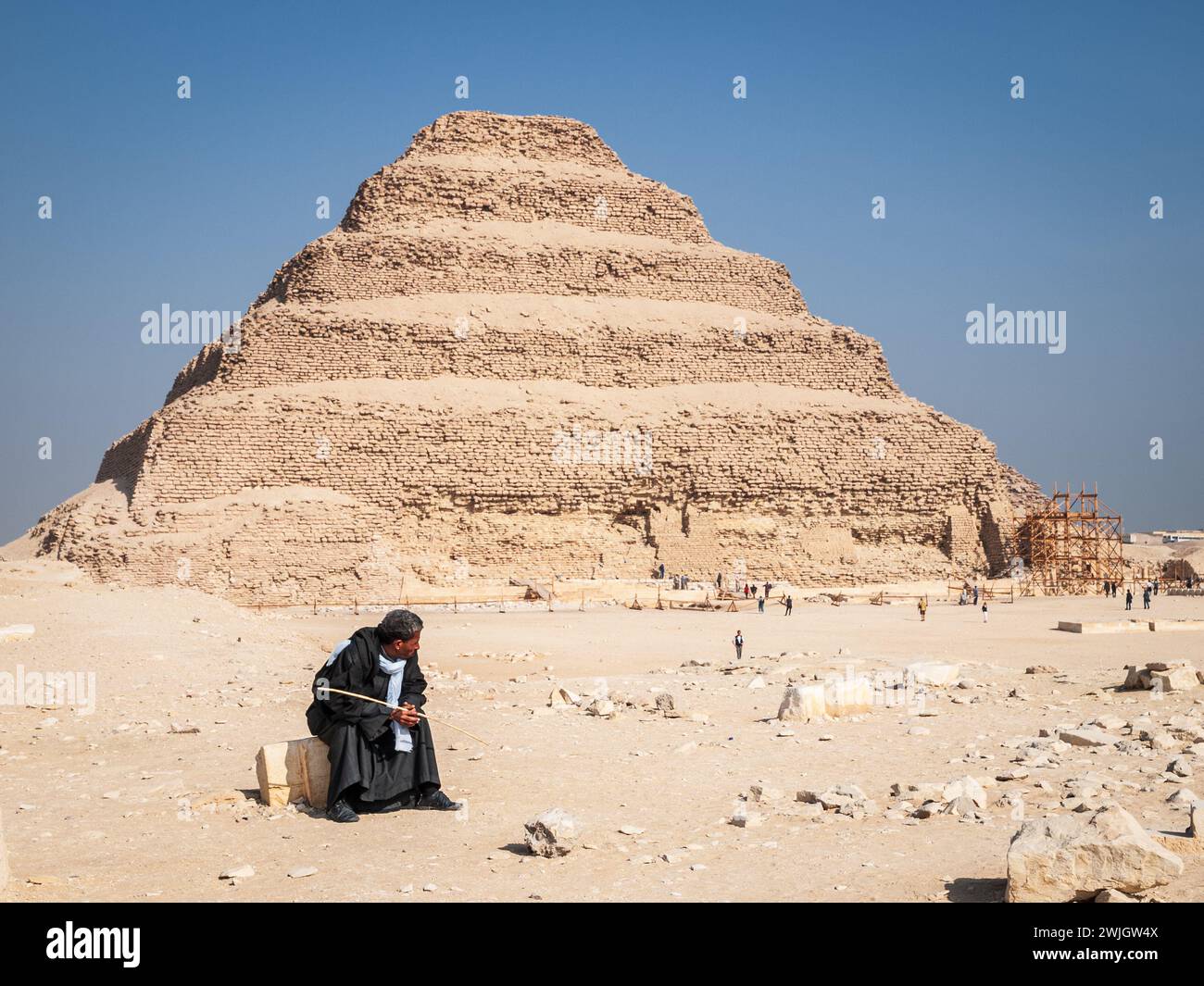 Egyptian man sitting in front of the step pyramid of Zoser on a sunny day, Saqqara necropolis, Giza, Egypt. Stock Photo