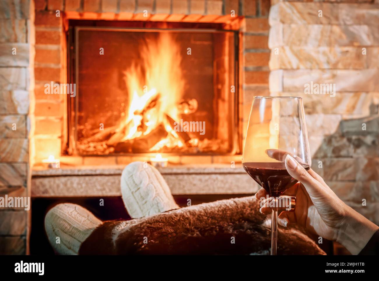Woman at the fireplace drinking a wine cup at home confort  - Selective focus. Stock Photo