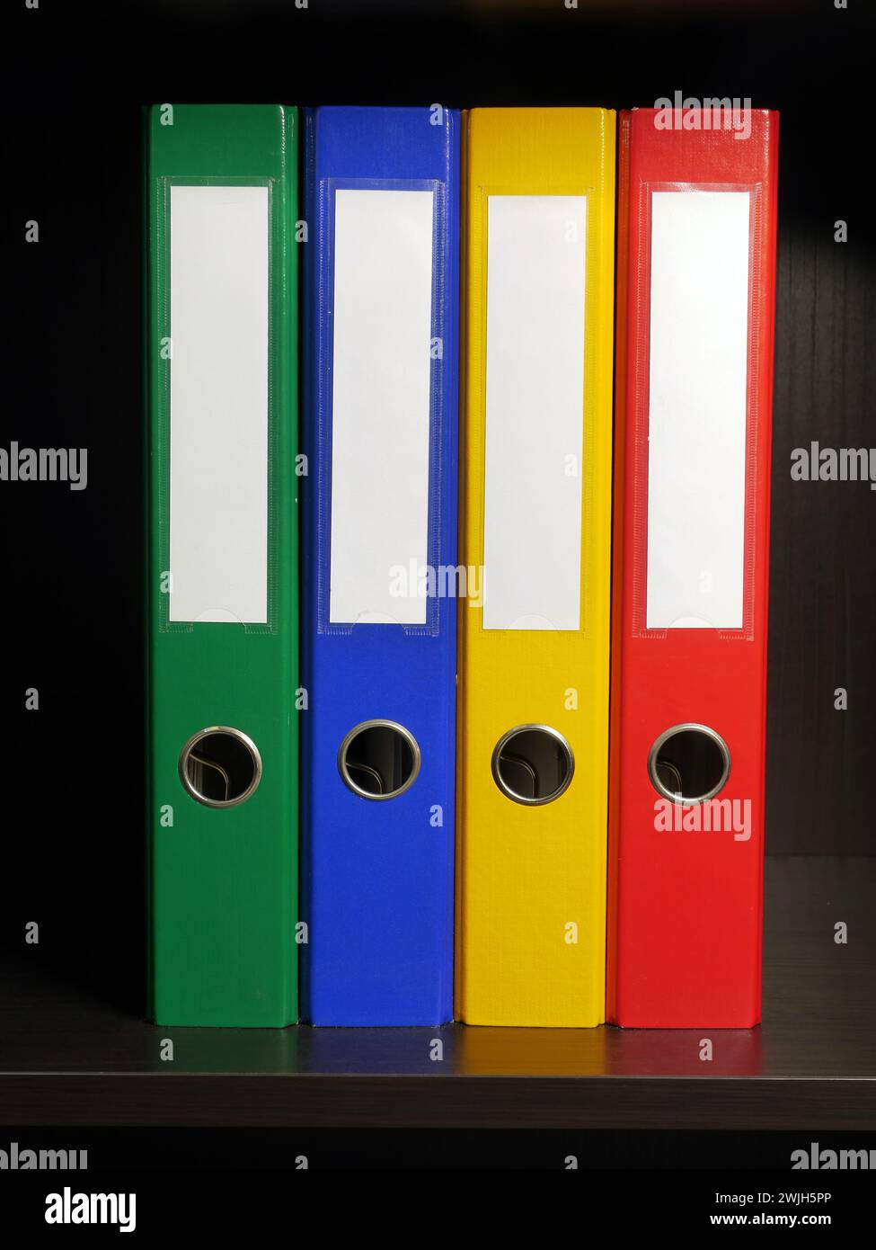 Four empty binders in green, blue, yellow and red colors arranged inside black cabinet Stock Photo