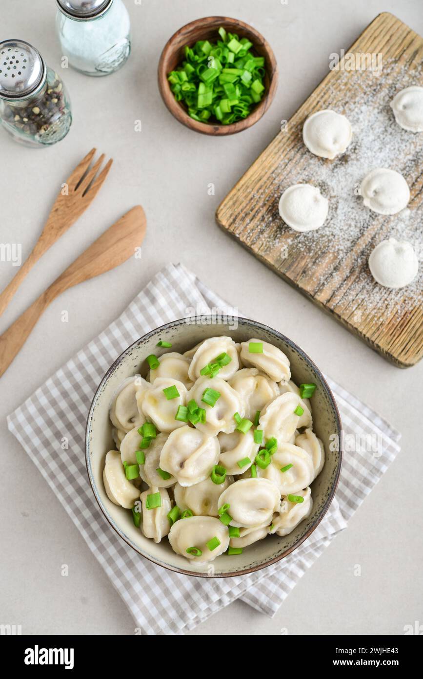 Russian pelmeni, dumplings with meat, butter and herbs on a light background, top view Stock Photo