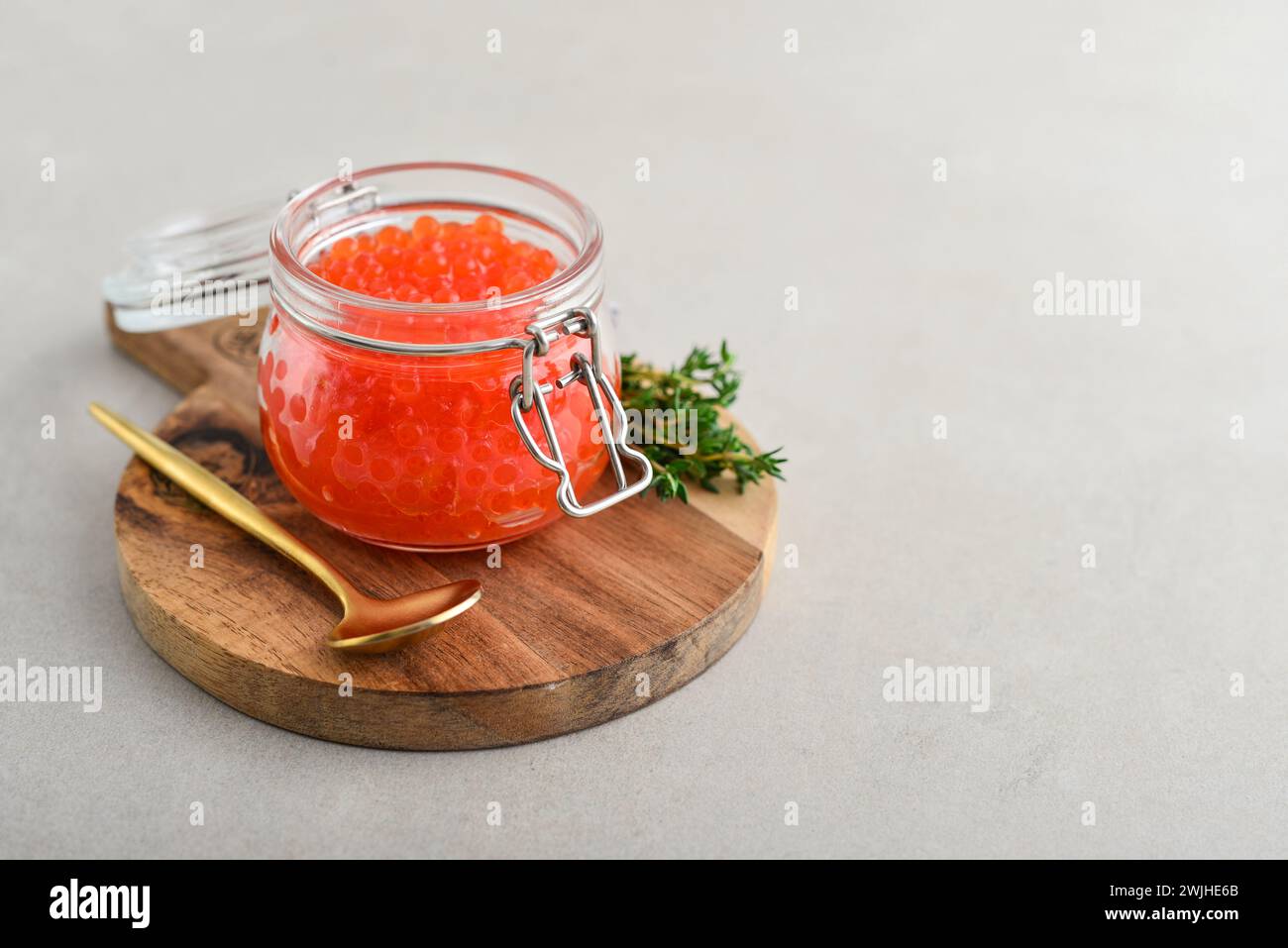 Red caviar in the glass jar on small wooden cutting board closeup Stock Photo