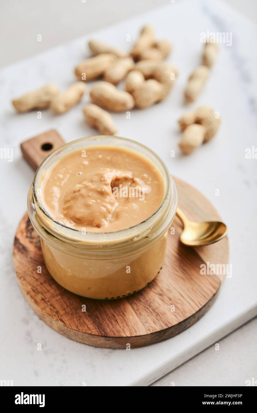 Creamy and smooth peanut butter in jar peanuts in shell on marble table. Natural nutrition and organic food. Stock Photo