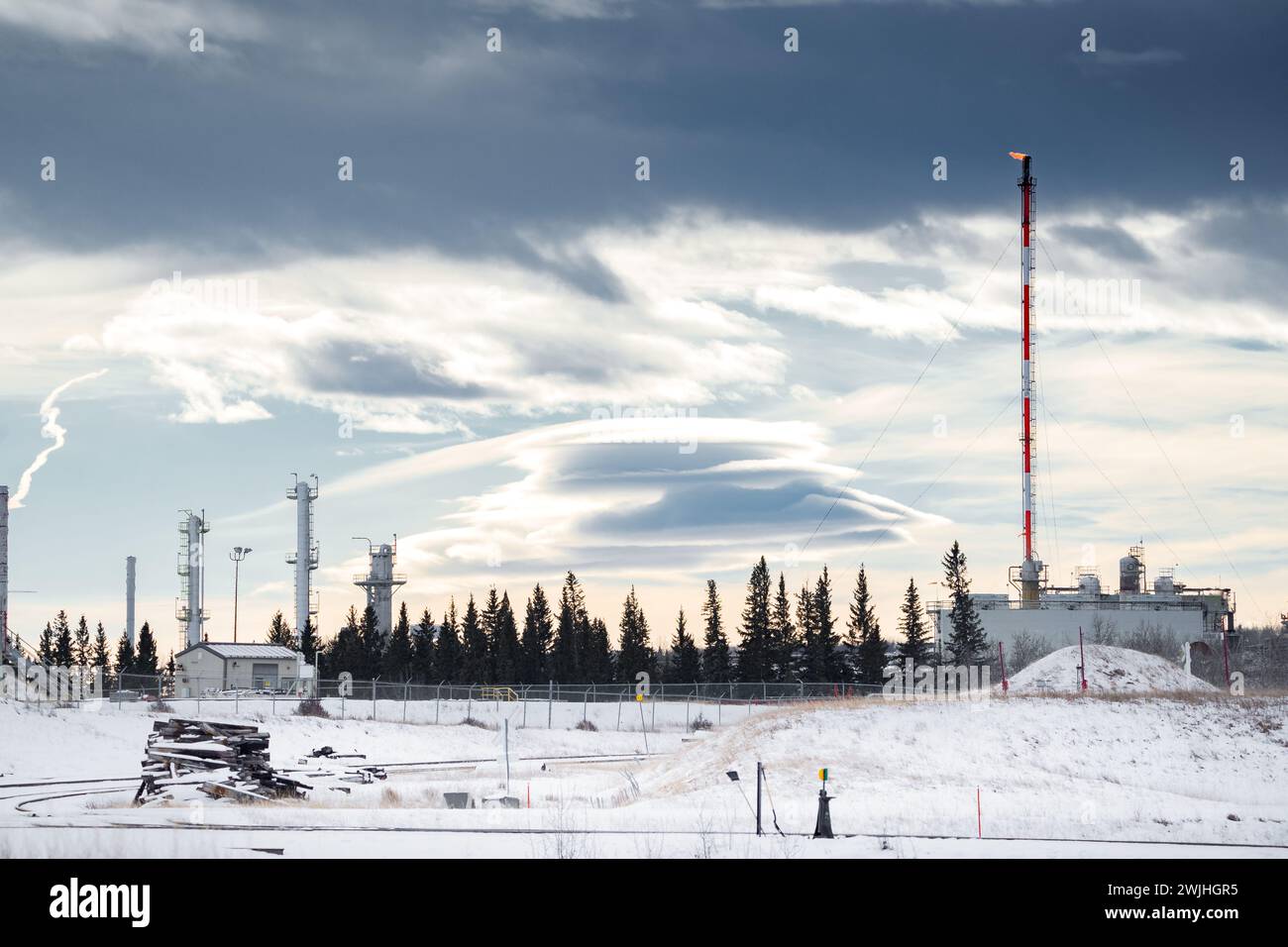 Oil and gas plant with a flare stack and flame under a dramatic winter sky in Western Canada. Stock Photo
