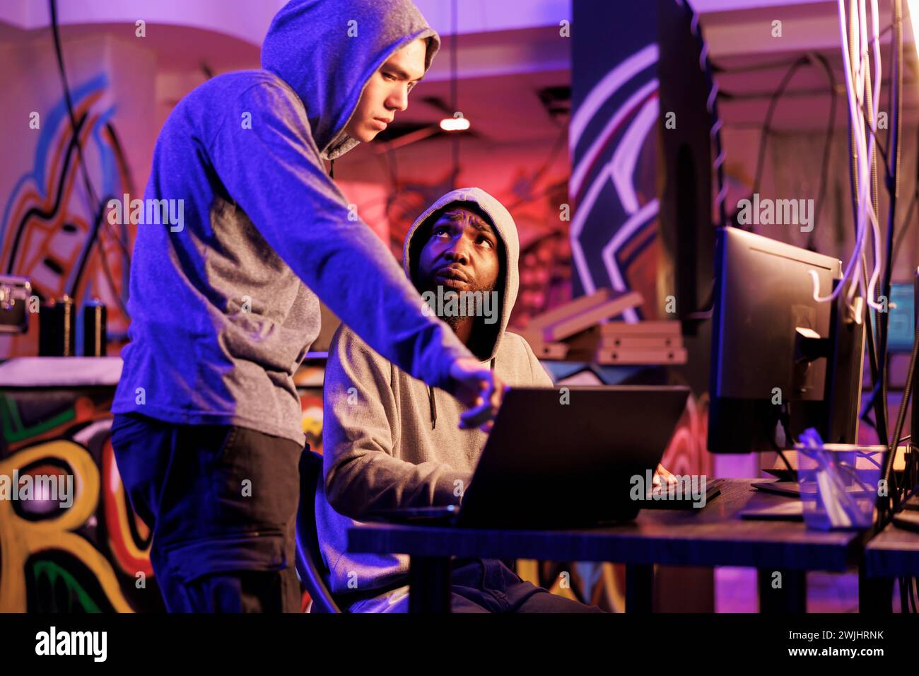 Hackers programming illegal malware on laptop and discussing code on screen. Criminals talking about cyberattack while breaking website on portable computer late at night Stock Photo