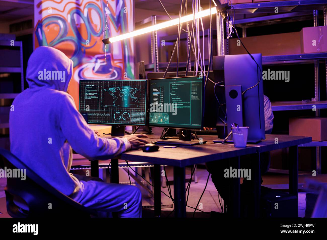 Hacker in hood gathering information using illegal spyware on computer to break into server. Criminal doing web tracking with malicious software and checking data on screen Stock Photo