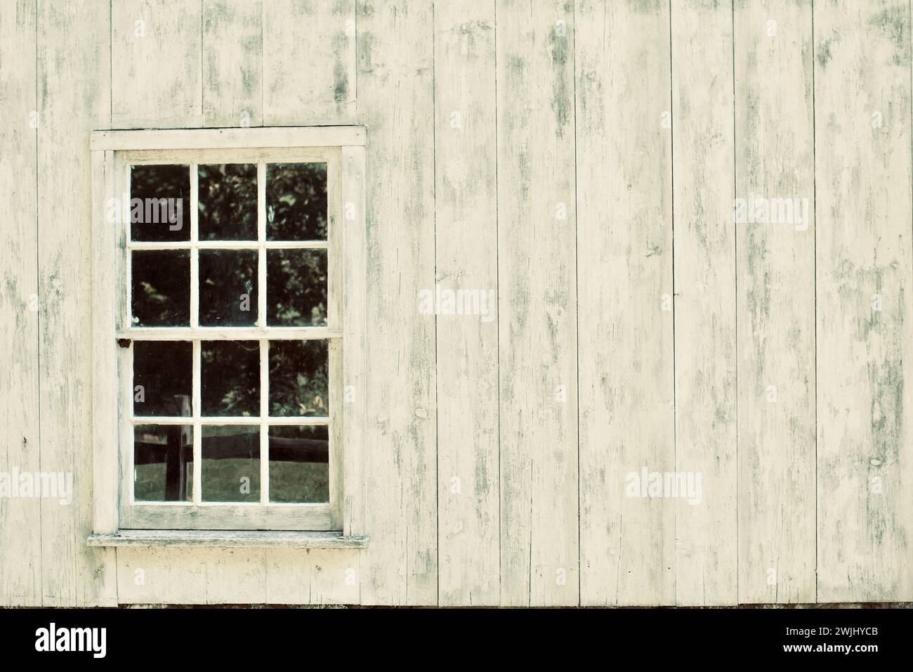 The side of a white barn with a glass six pane window to the left. Stock Photo