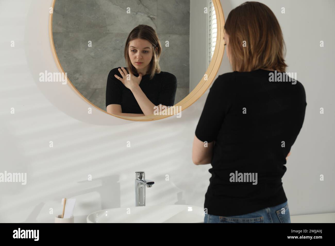 Sad young woman near mirror in bathroom Stock Photo