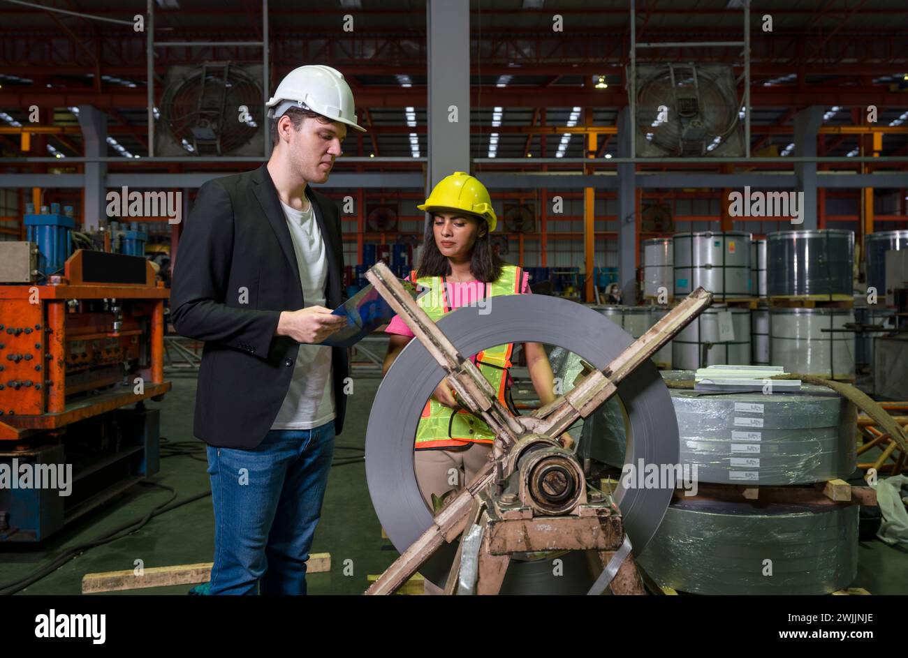 Two people wearing hard hats standing next to a large roll forming machine wheel in an industrial factory. Stock Photo