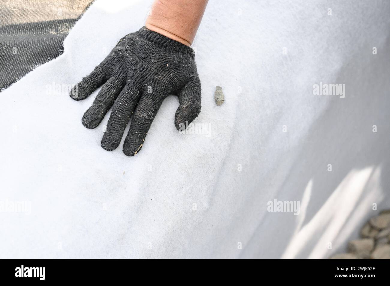 The craftsman spreads white geotextile in the trench. A mans hand in black gloves on a white canvas. Stock Photo