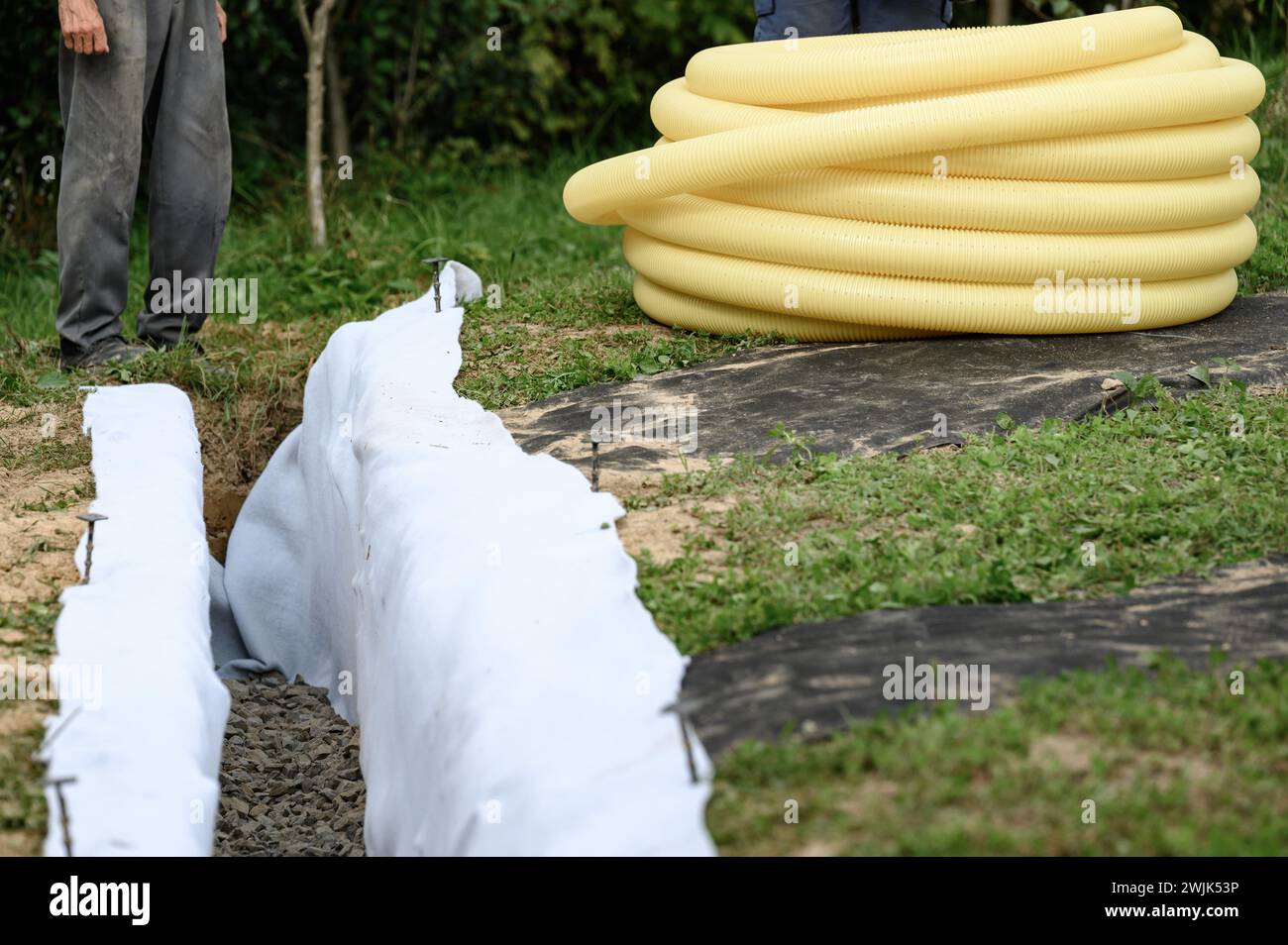 Workers carry a roll of yellow drainage pipe in their hands. Preparation for drainage works and removal of groundwater. Stock Photo