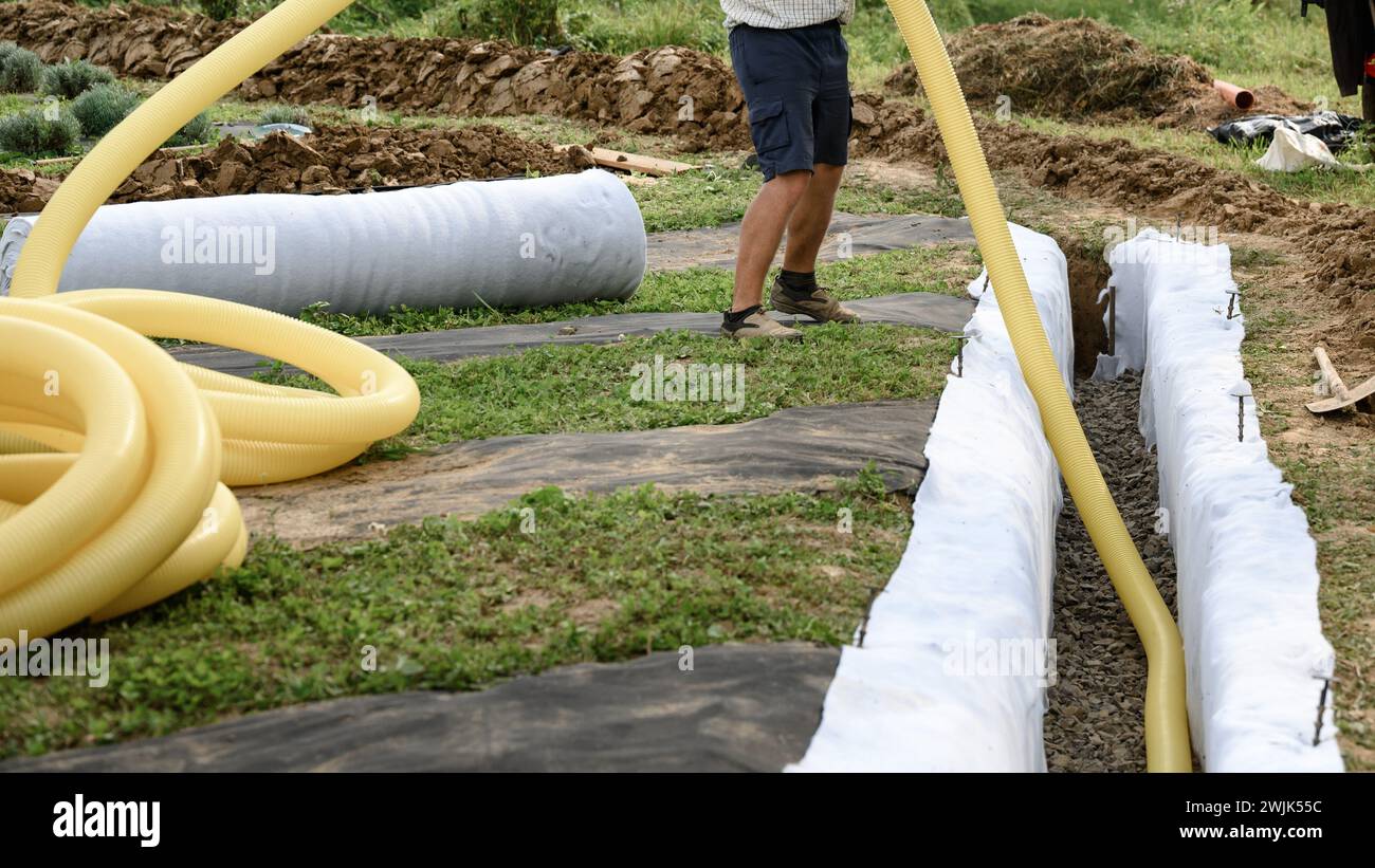 Groundwater drainage works in the field. A worker carries a yellow perforated drainage pipe. Stock Photo