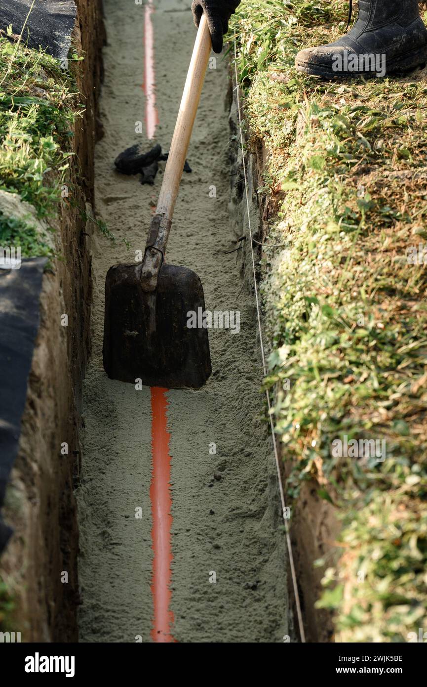 A plumber installs a reinforced orange sewer pipe during site maintenance. Stock Photo