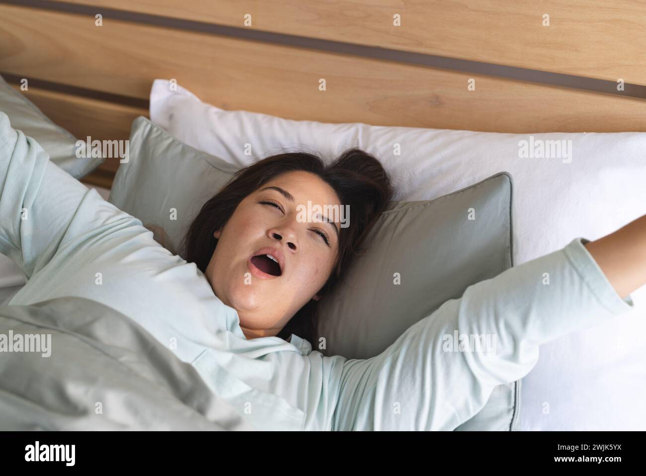 Young plus size biracial woman stretching in bed at home, with copy space Stock Photo