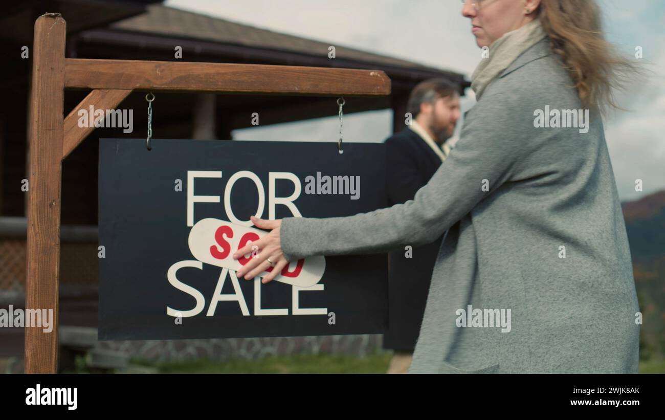 Female real estate agent puts sold sticker on for sale sign and ...