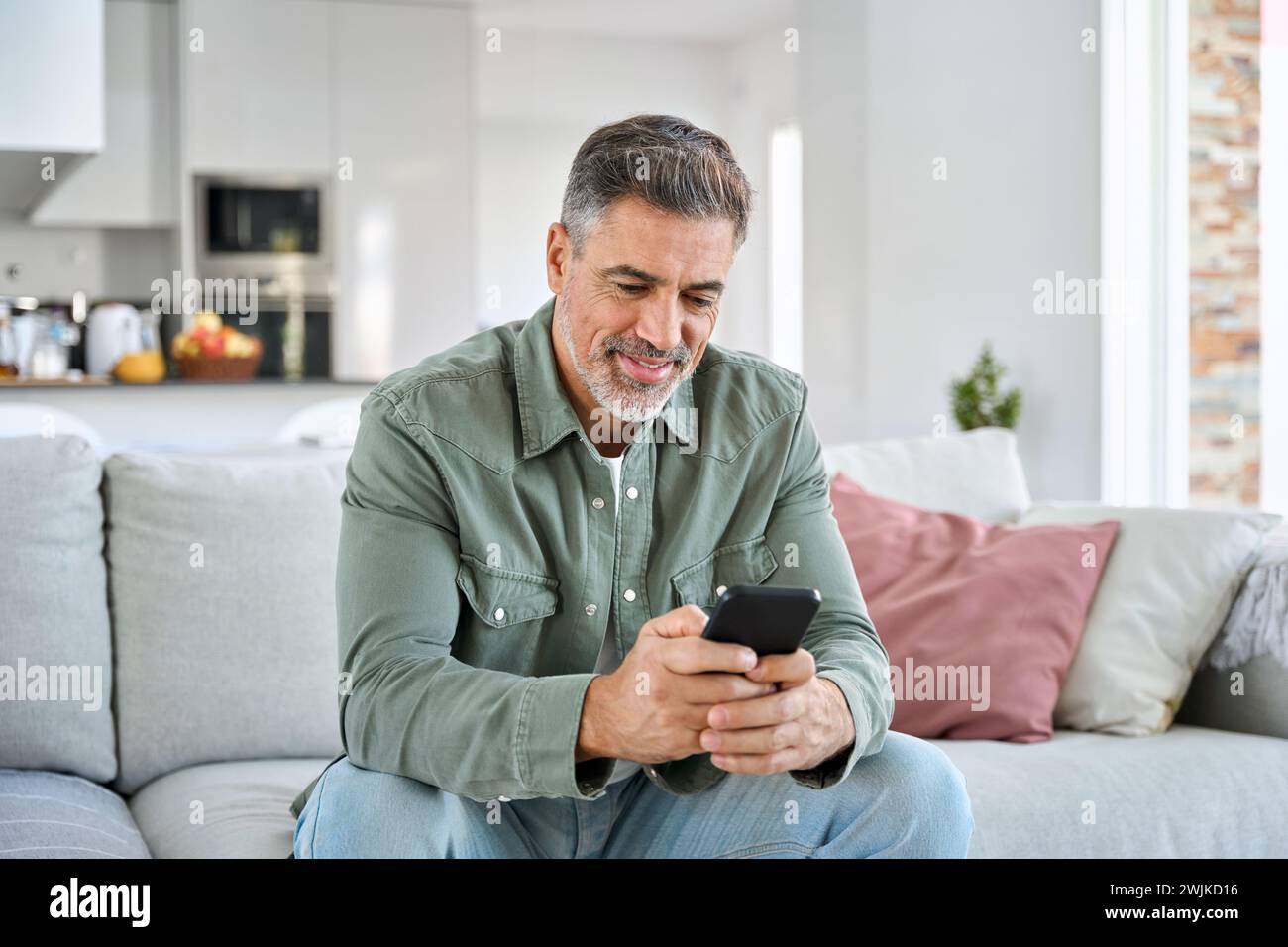 Middle aged old man using smartphone relaxing on couch at home. Stock Photo