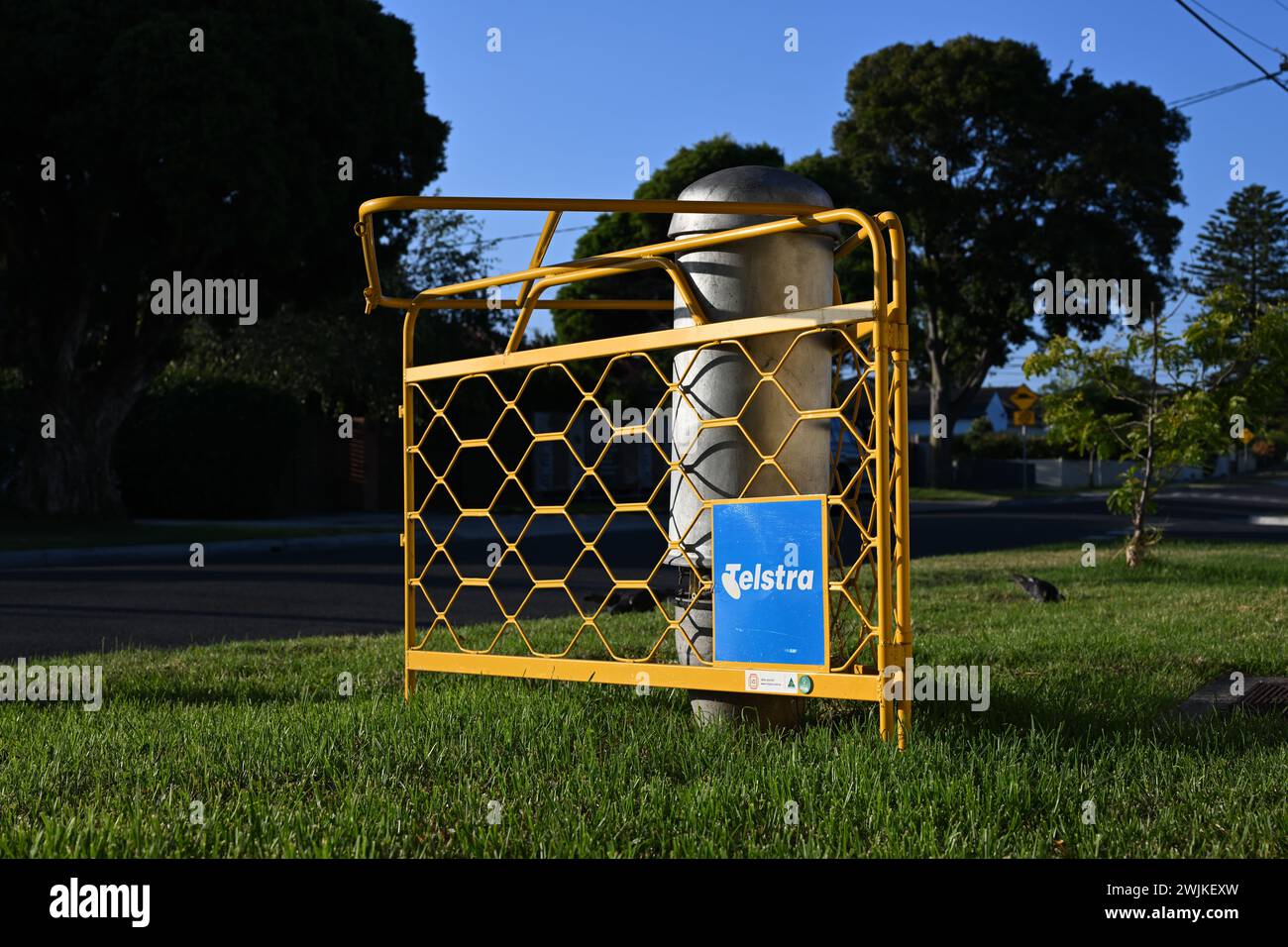 Telstra communication pillar on a suburban nature strip, guarded by a yellow barrier featuring a faded Telstra logo Stock Photo