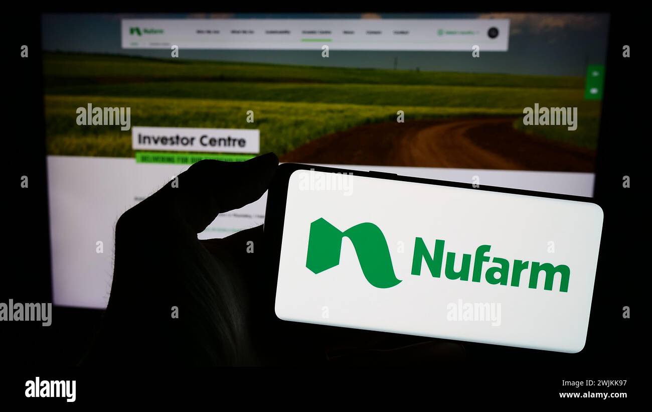 Person holding mobile phone with logo of Australian agrochemical company Nufarm Limited in front of business web page. Focus on phone display. Stock Photo