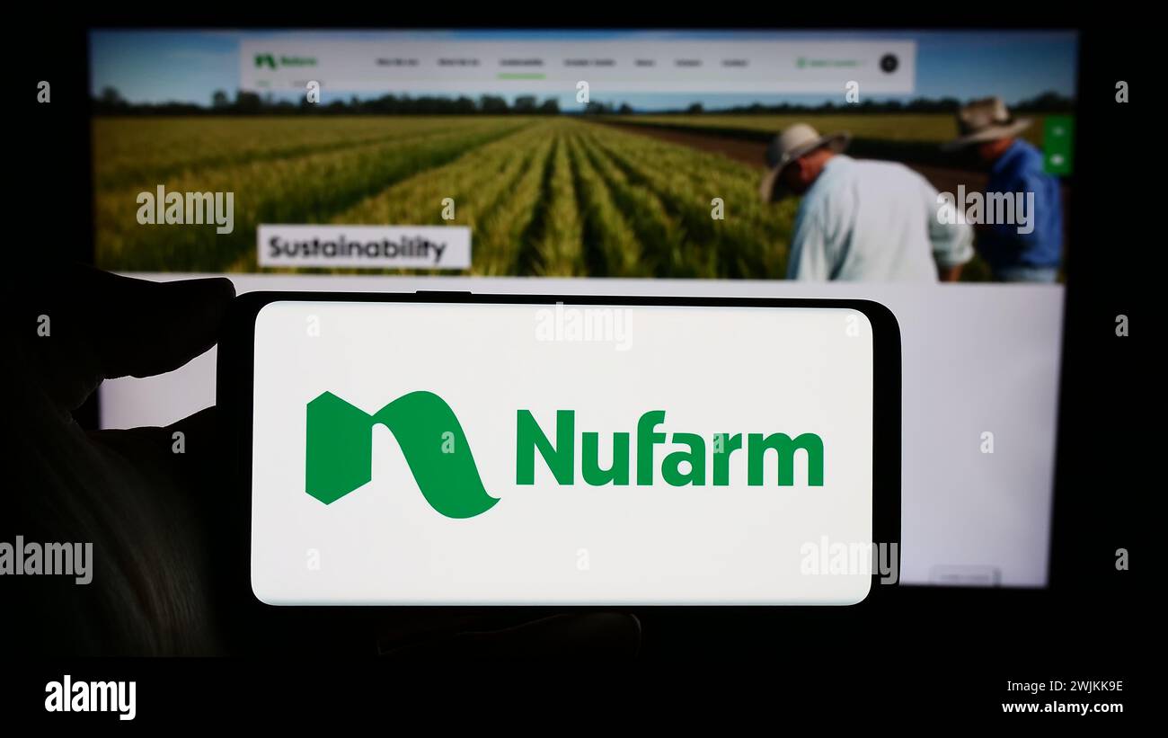 Person holding cellphone with logo of Australian agrochemical company Nufarm Limited in front of business webpage. Focus on phone display. Stock Photo