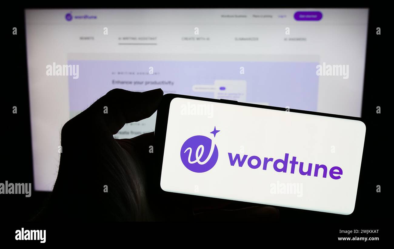 Person holding smartphone with logo of artificial intelligence companion Wordtune (AI21 Labs) in front of website. Focus on phone display. Stock Photo