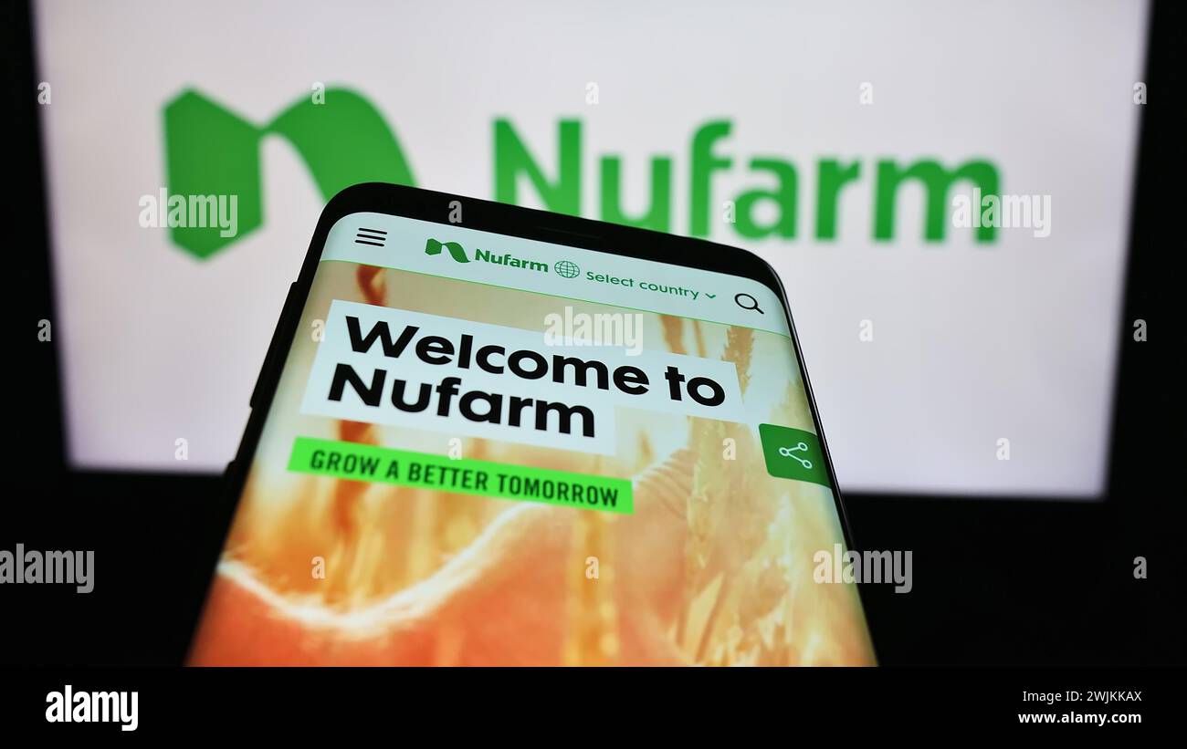 Mobile phone with webpage of Australian agrochemical company Nufarm Limited in front of business logo. Focus on top-left of phone display. Stock Photo