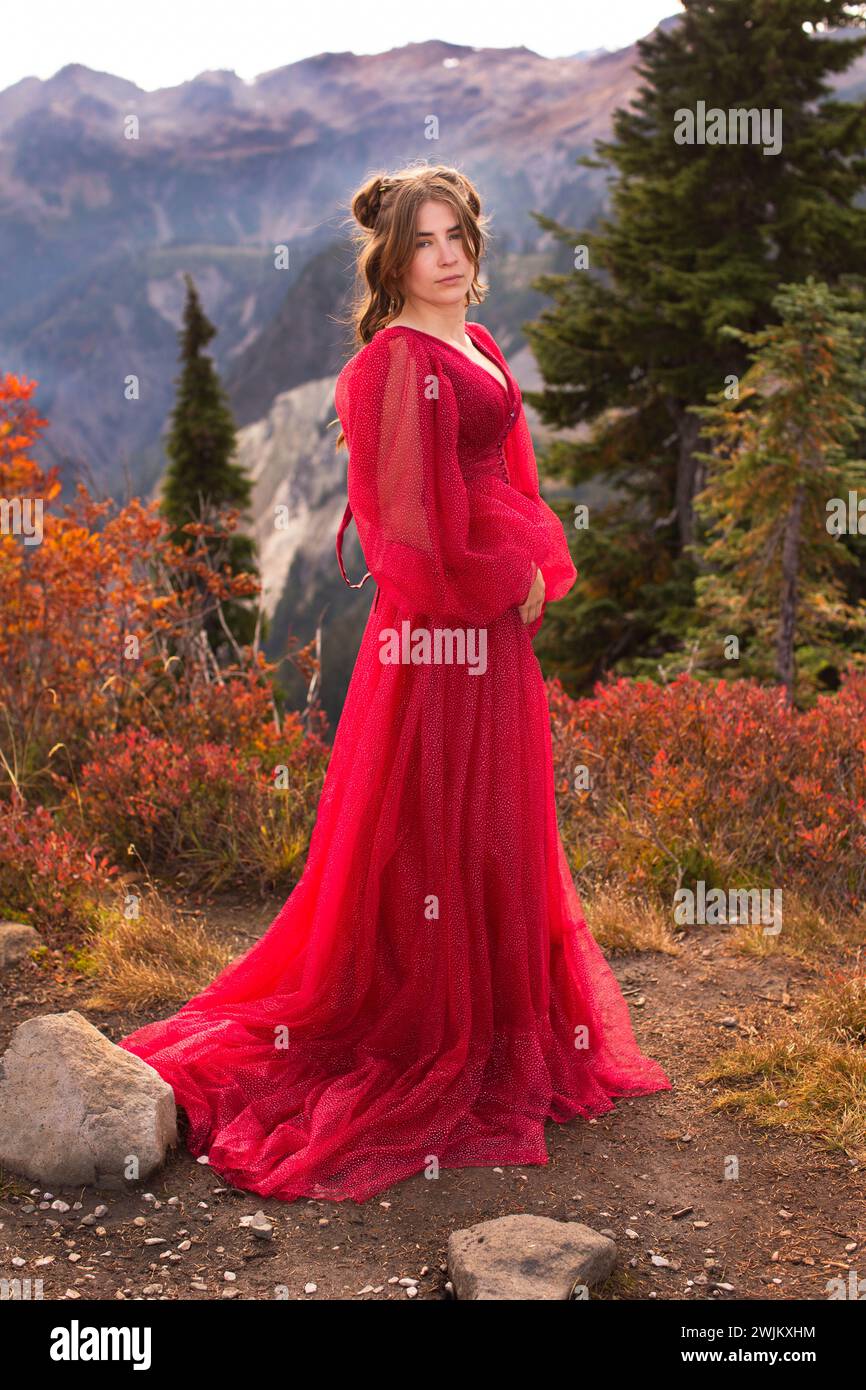 Strong serious woman in red gown on mountain Stock Photo