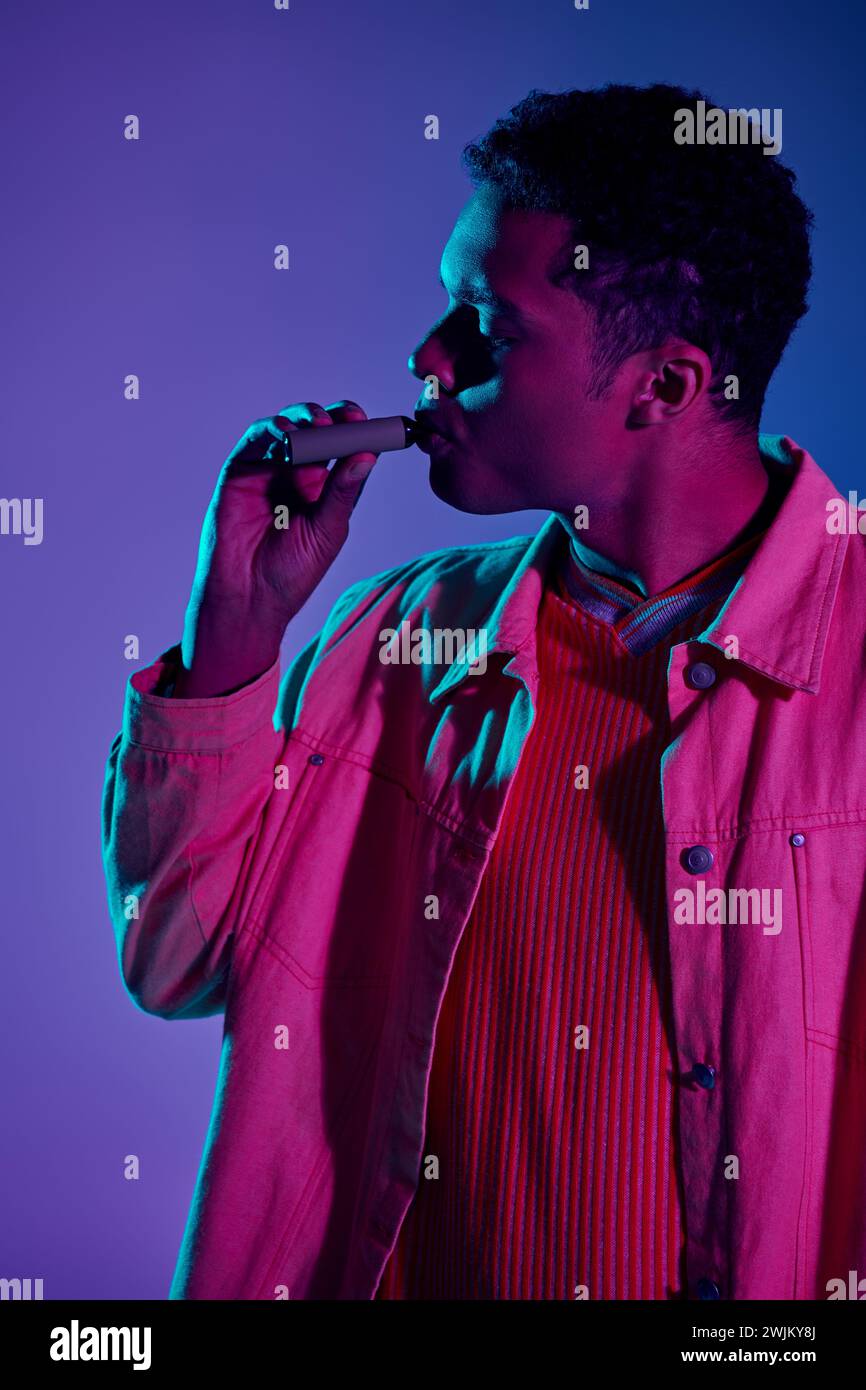 young african american man vaping electronic cigarette on grey backdrop with colorful lighting Stock Photo