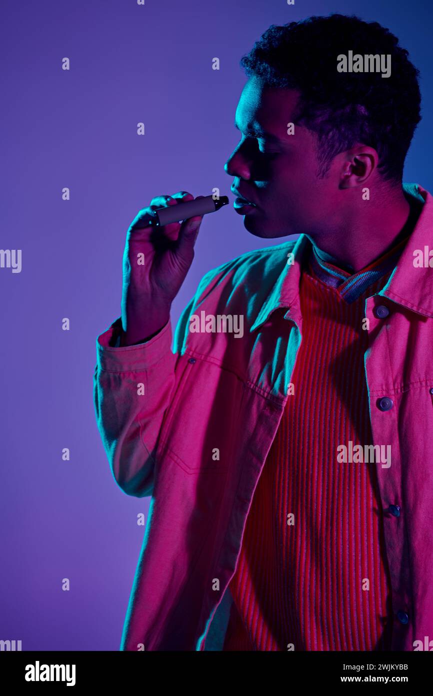 african american guy vaping with electronic cigarette in hand, grey backdrop with lighting Stock Photo