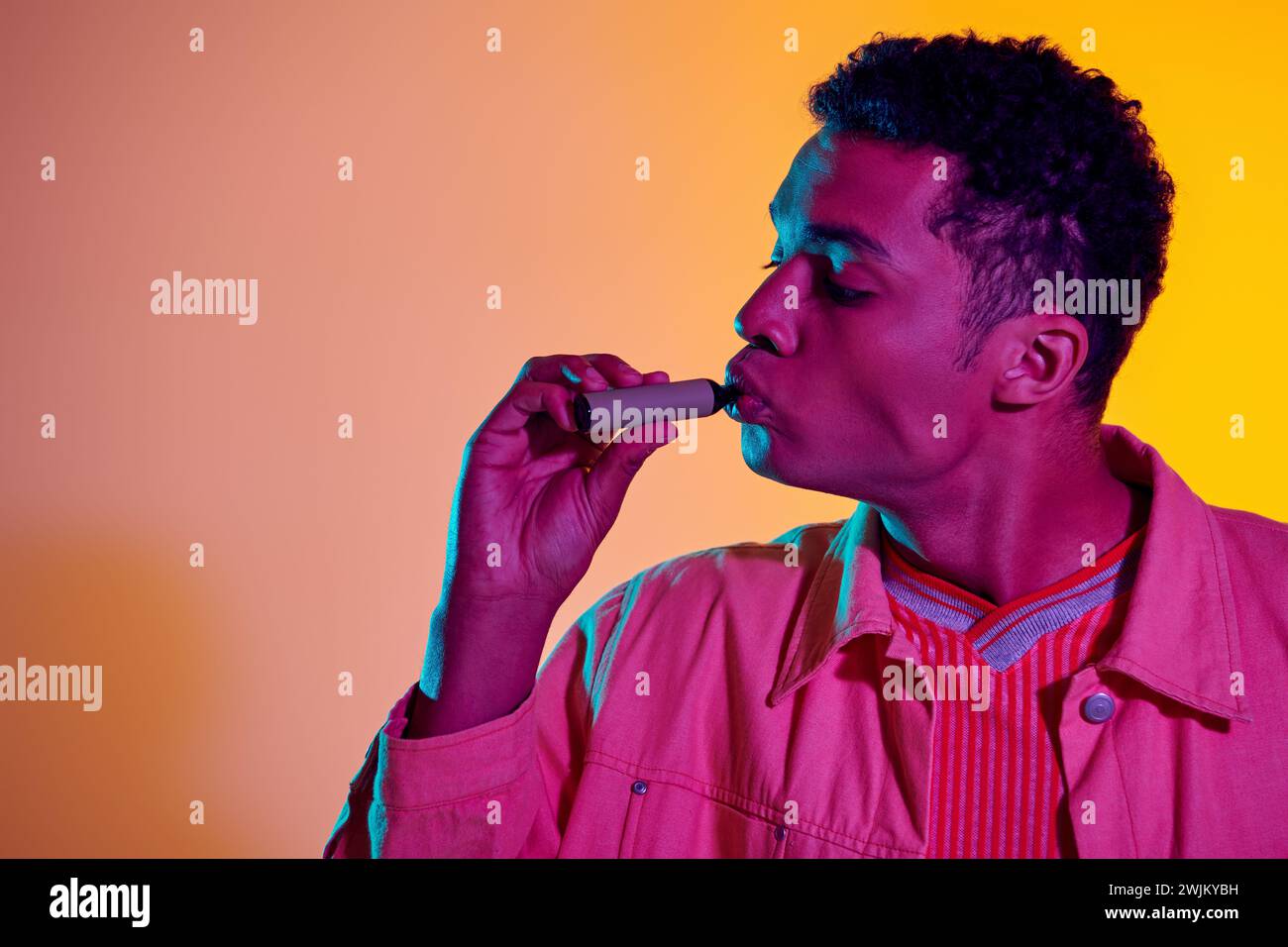 african american man with electronic cigarette against colorful backdrop with lighting, vaping Stock Photo