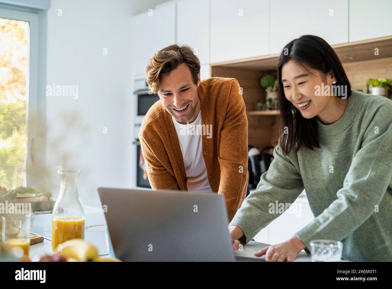 Adult couple shopping online on laptop while leaning on kitchen counter Stock Photo
