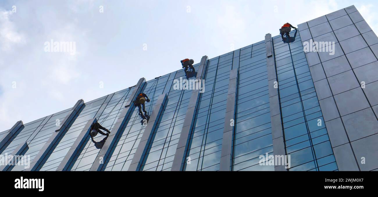 Employee cleaning the glass of a high-rise building city office Abseiling from the roof of a building Stock Photo