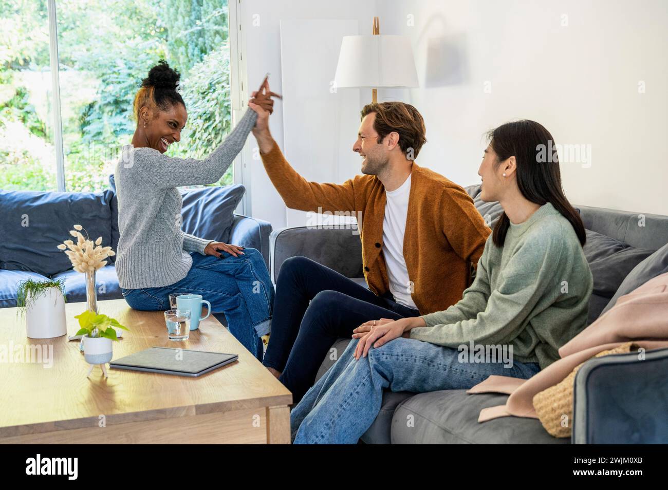 Adult man high fiving with friend during reunion at living room Stock Photo