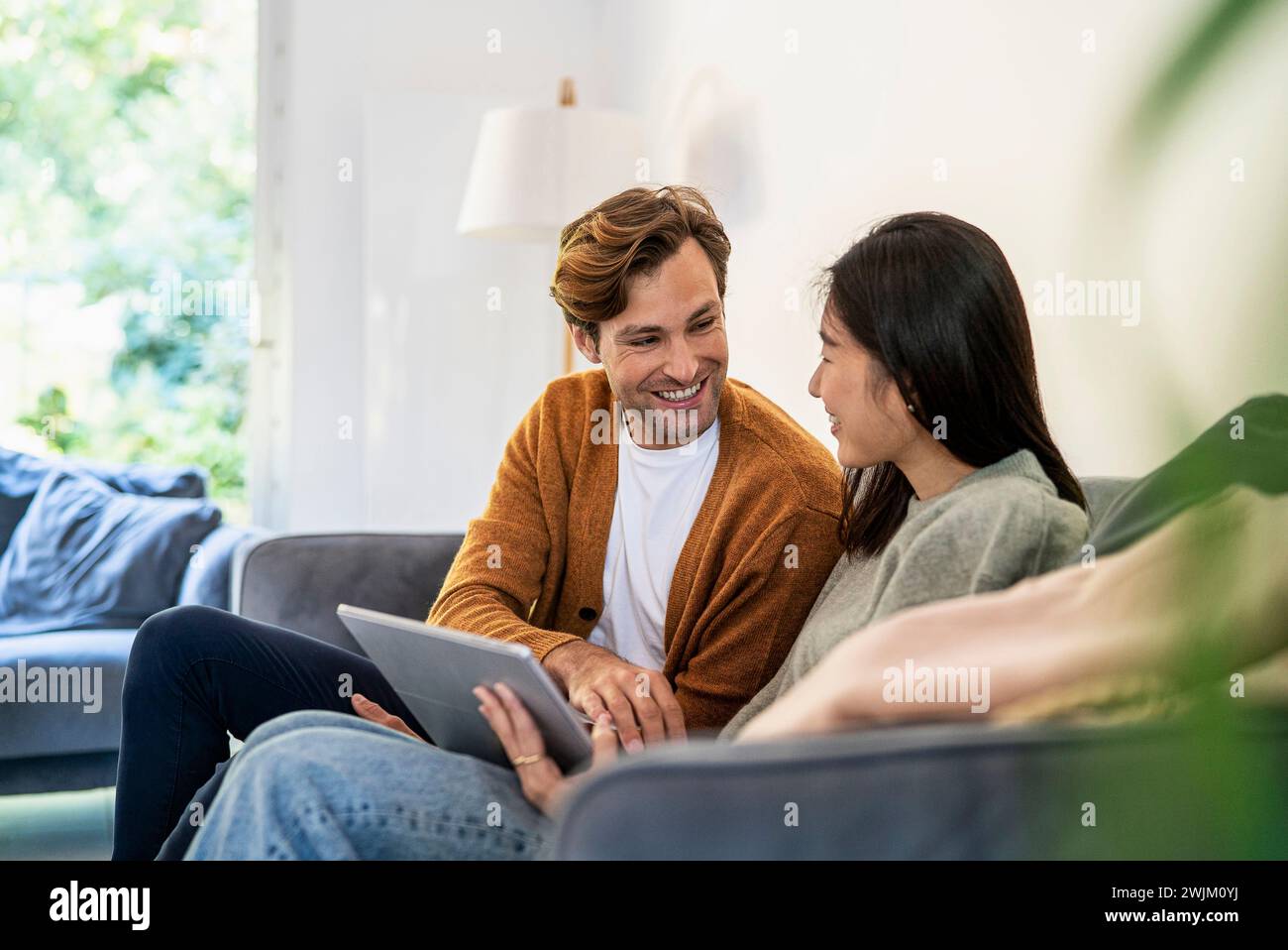 Adult couple having fun while using digital tablet sitting on sofa Stock Photo