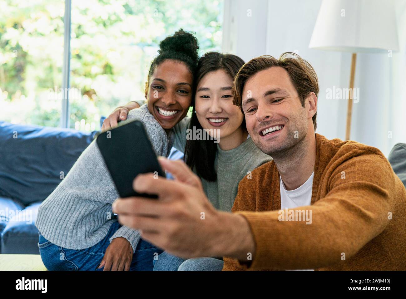 Small group of friends taking a selfie while sitting on sofa Stock Photo
