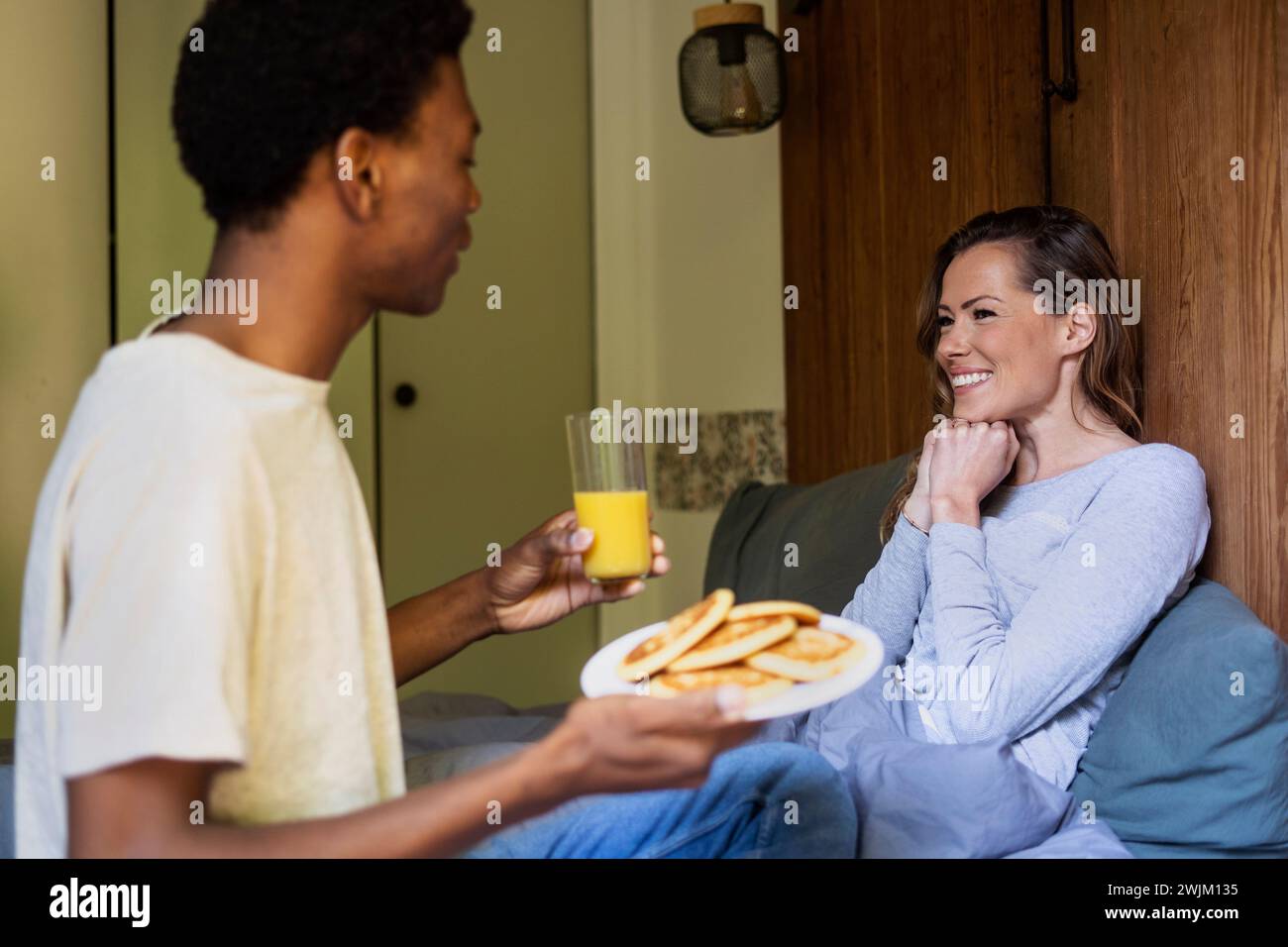 Happy woman lying on bed while boyfriends surprised her with breakfast Stock Photo