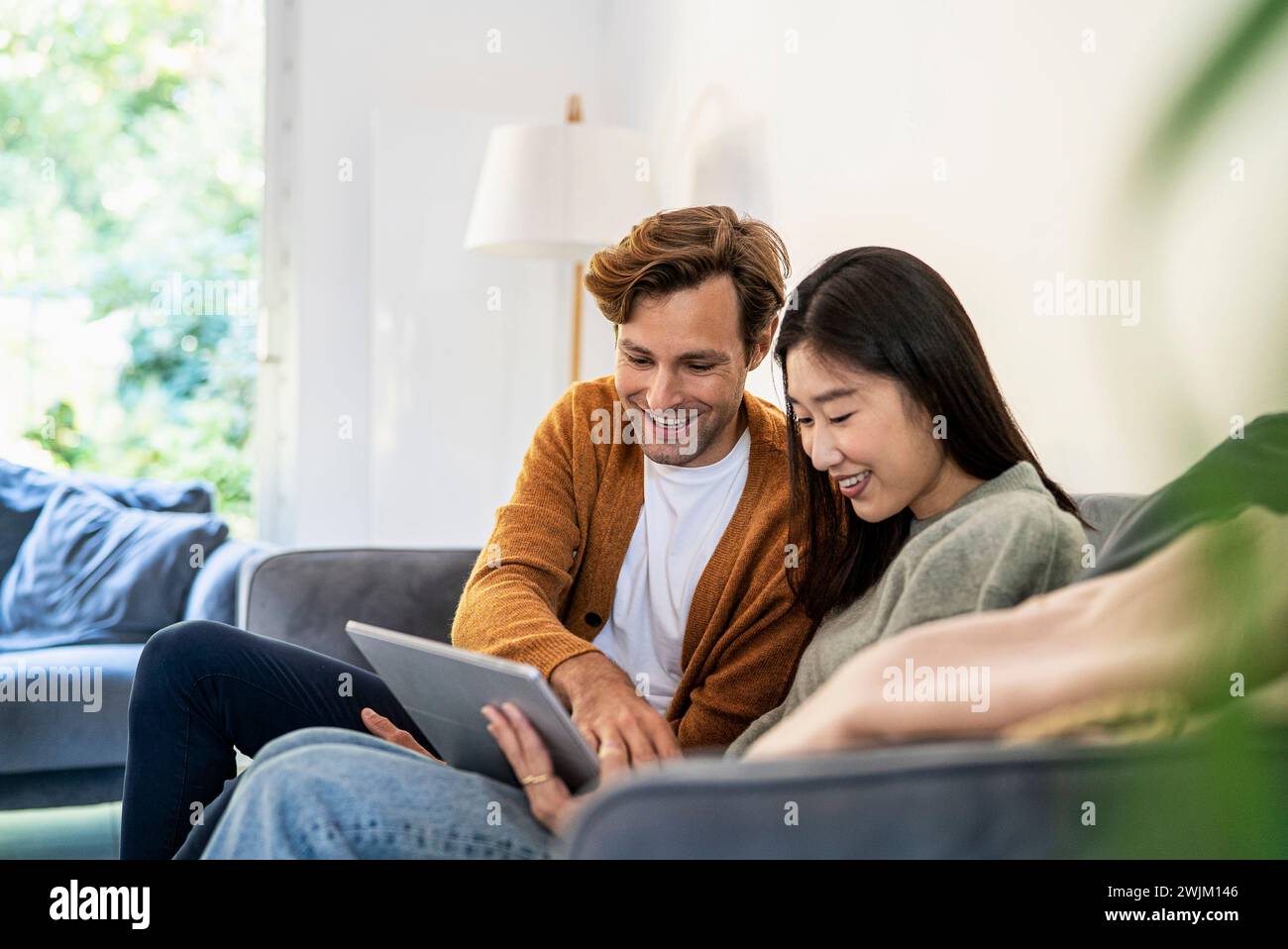 Adult couple using digital tablet while sitting on sofa Stock Photo