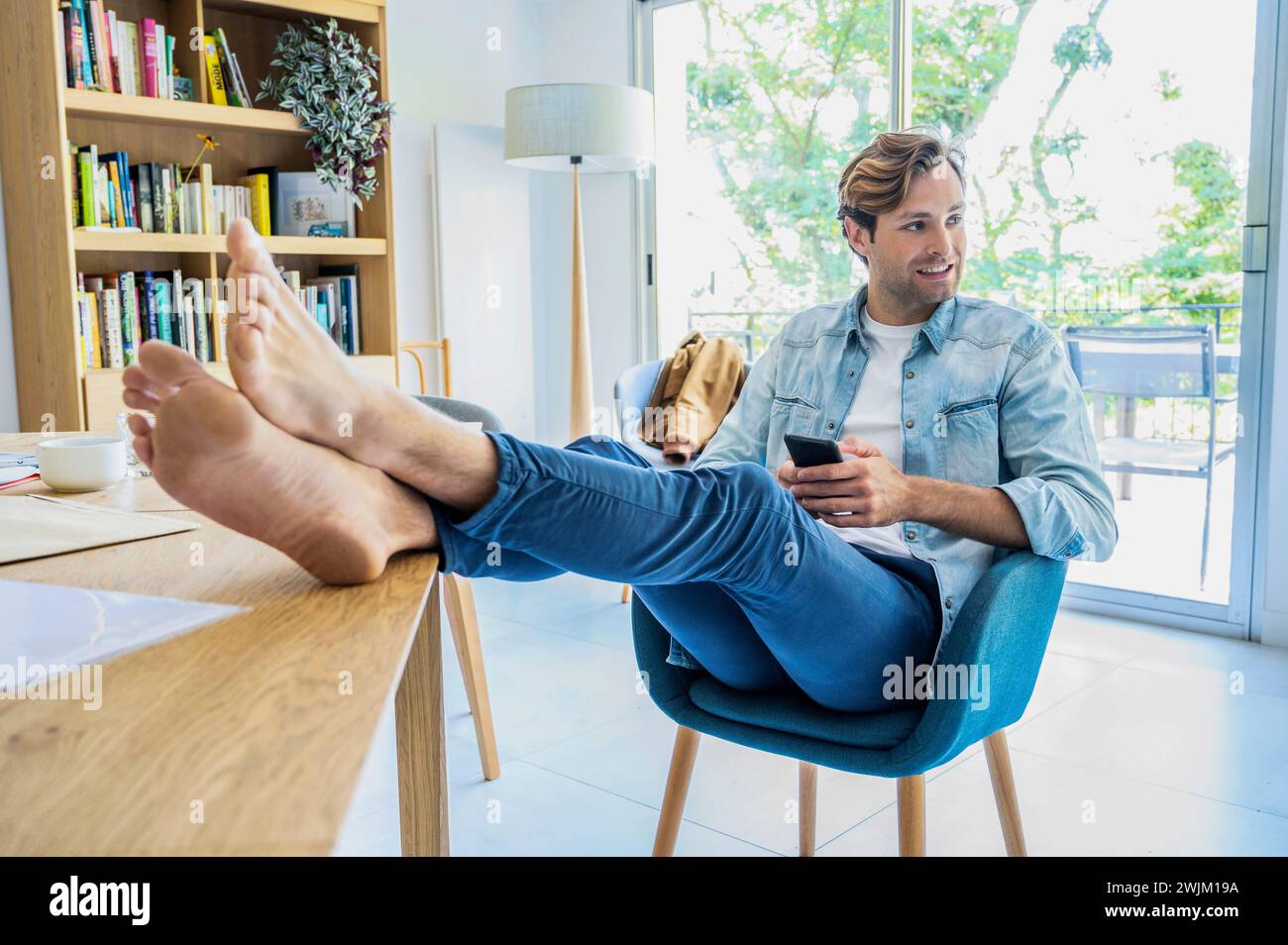 Young adult man resting feet while working with smart phone at home Stock Photo