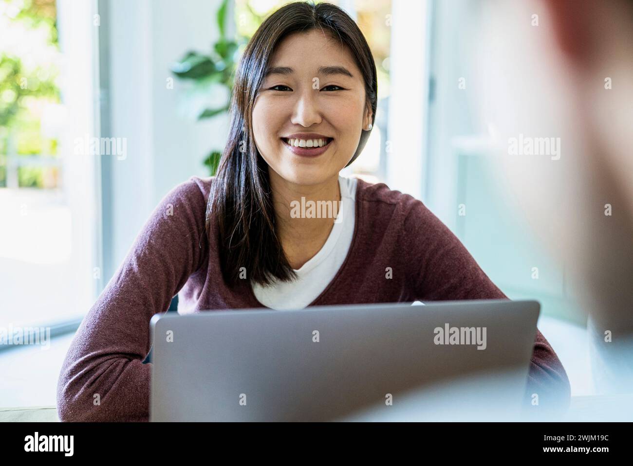 Young adult coworker using laptop while looking at the camera Stock Photo